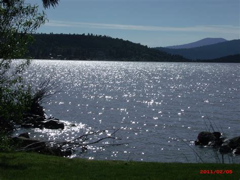 the sun shines brightly on the water near some trees and mountains in the distance