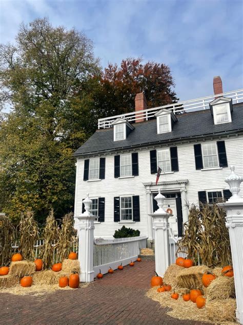 a large white house with pumpkins in the front yard and hay bales on the ground