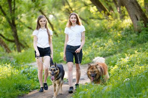 Two teenage girls walking with her dogs in park | High-Quality People Images ~ Creative Market