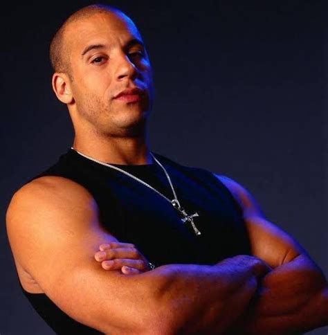 a man with his arms crossed wearing a black shirt and silver cross pendant on his necklace