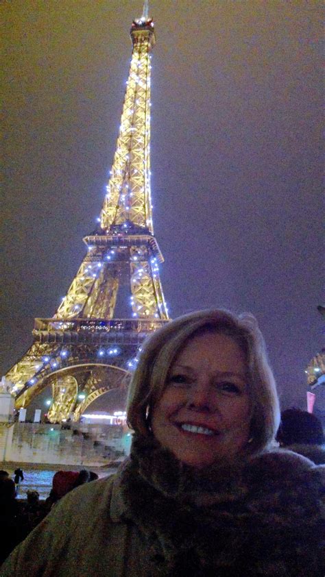 a woman standing in front of the eiffel tower at night with lights on