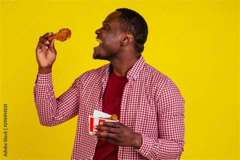 funny african american man eating fried chicken leg in studio yellow ...