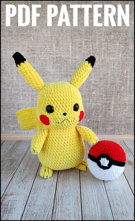 a crocheted pikachu doll next to a pokemon ball on a wooden table