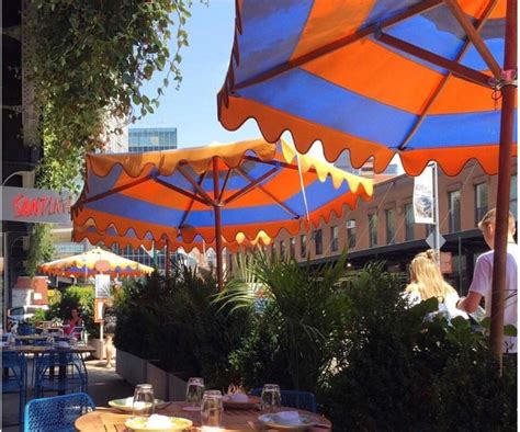 an outdoor dining area with blue and orange umbrellas over tables, people sitting at the tables