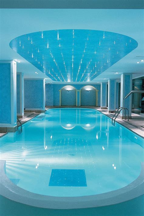 a large indoor swimming pool with blue walls and water features in the center, along with steps ...
