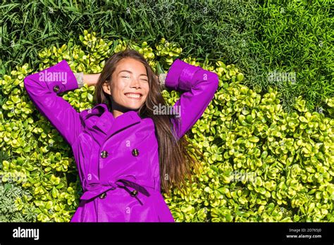 Happy spring girl lying on green grass texture background. Asian woman wearing purple trench ...