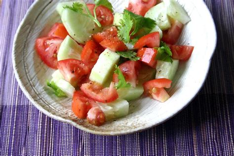 a white bowl filled with cucumber, tomato and cilantro on top of a purple place mat