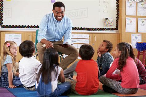 Elementary school kids sitting around teacher in a classroom - Stock Photo - Dissolve