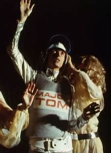 A man wearing a space suit emblazoned "Major Tom" floats in a black void with two women in ...