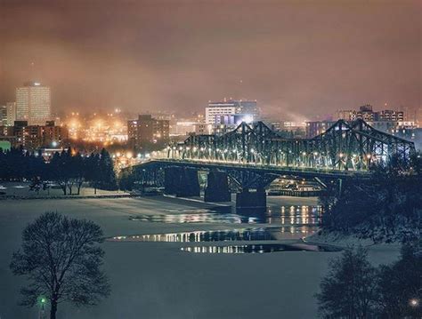 a bridge that is over some water in the night time with city lights behind it