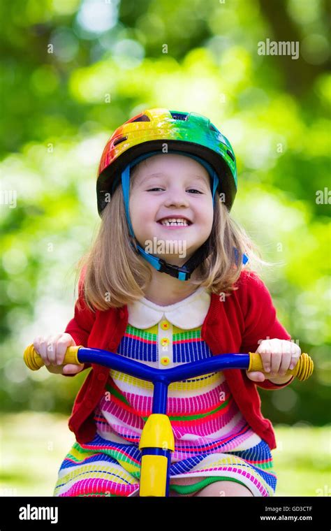 Cute girl wearing safety helmet riding her tricycle in sunny summer ...