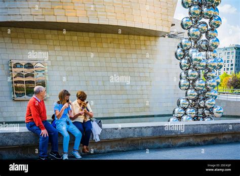 Tourists Resting Next To The Facade Of The Guggenheim Museum Bilbao