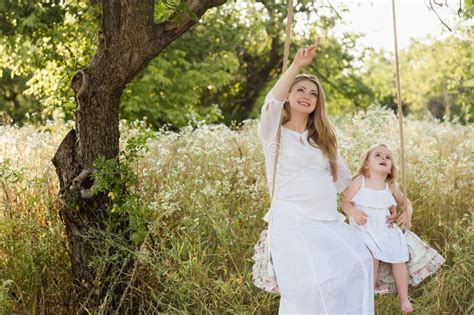 Belle Mère Enceinte Avec La Petite Fille Blonde Dans Une Robe Blanche Se Reposant Sur Une