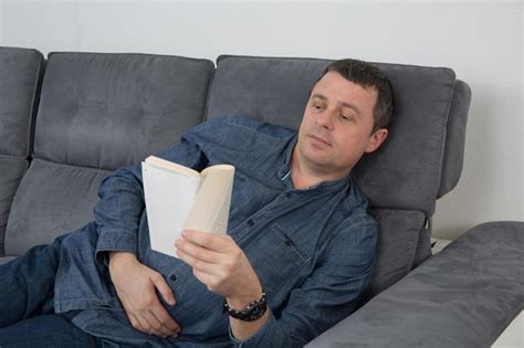 Hombre sonriente leyendo un libro y relajándose en el sofá Foto Premium