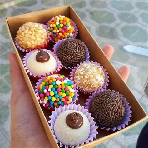 A Hand Holding A Box Filled With Different Types Of Cupcakes