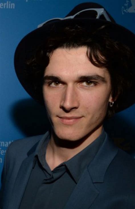 A Man Wearing A Black Hat Standing In Front Of A Blue Wall