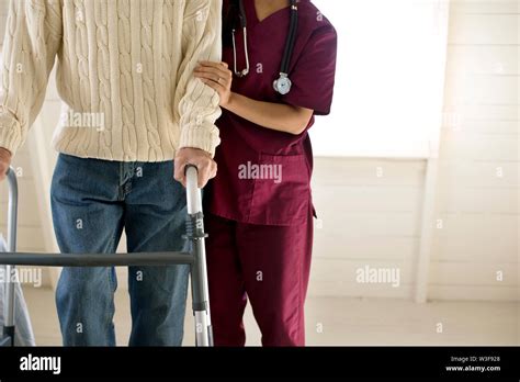 Female Nurse Encouraging An Elderly Male Patient To Use A Walking Frame