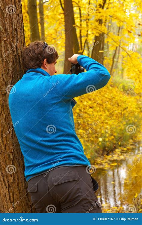 Man Leaning Against A Tree And Taking Photo Of An Autumnal Fores Stock