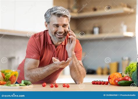 Happy Middle Aged Man Having Phone Conversation While Cooking Stock