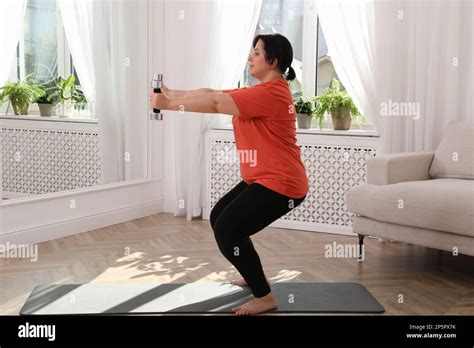 Overweight Mature Woman Doing Exercise With Dumbbells At Home Stock