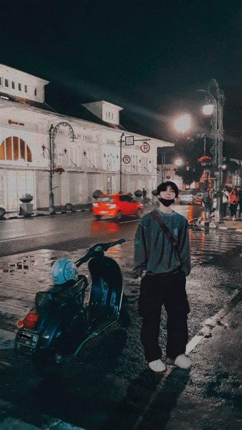 A Man Standing Next To A Motorcycle On A Wet Street At Night With