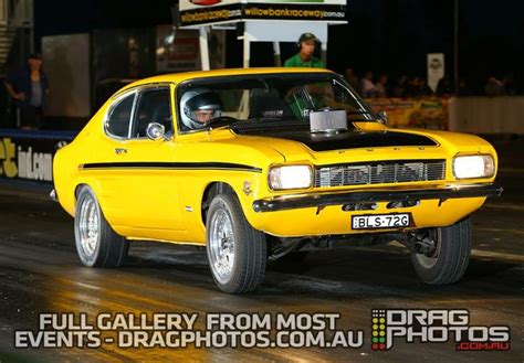 A Yellow Car Driving Down A Street At Night With People Watching From