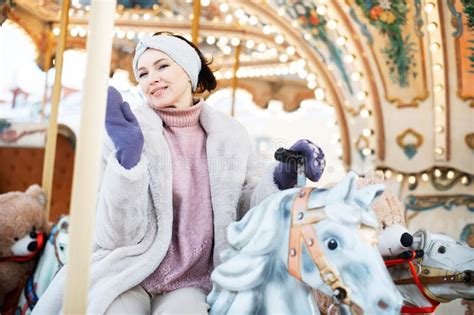 Beautiful And Cheerful Brunette Woman In A Fur Coat Rides On A Carousel