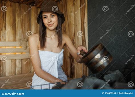 Portrait Of A Beautiful Girl With A Wooden Ladle In The Sauna Pouring Water On Hot Stones Stock