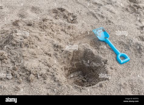 Seaside hole dug into sand, with kids blue spade. Metaphor 'dig a hole ...