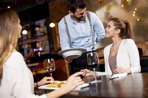 Joven Mesero Sirviendo Comida A Clientas En El Restaurante