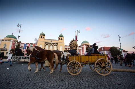 Two Horses Pulling A Cart With People In It On A Cobblestone Street