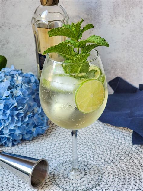 A Glass Filled With Lemonade And Mint On Top Of A Table Next To A Bottle