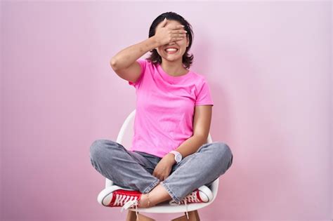 Jeune Femme Hispanique Assise Sur Une Chaise Sur Fond Rose Souriant Et