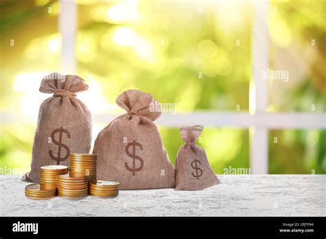 Burlap Bags With Dollar Signs And Coins On White Table Indoors Stock