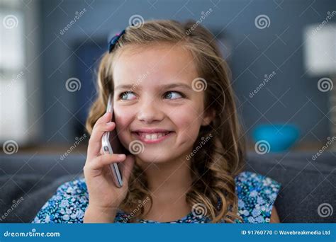 Menina Feliz Que Fala No Telefone Celular Na Sala De Visitas Foto De