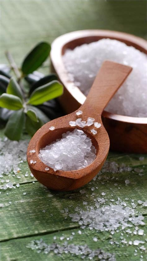 Sea Salt In A Wooden Spoon Next To An Olive Branch On A Green Wood Table