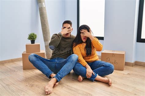 Young Couple Sitting On The Floor At New Home Peeking In Shock Covering