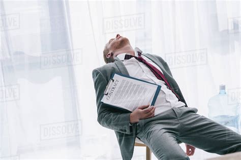 Exhausted Businessman Sleeping On Chair With Contract In Hand At Office