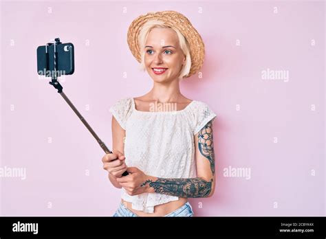 Junge blonde Frau mit Tattoo nimmt ein Selfie Foto mit Smartphone sieht positiv und glücklich
