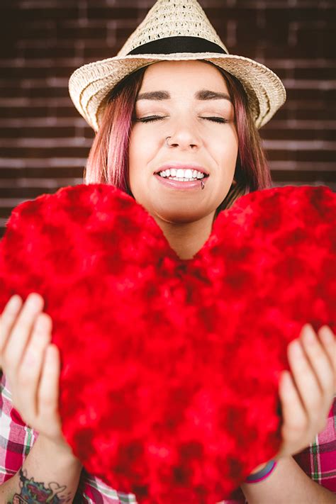 Smiling Woman Holding Heart Shape Against Brick Wall