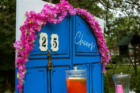 A Blue Door Decorated With Pink Flowers Next To A Drink Dispenser And Glass