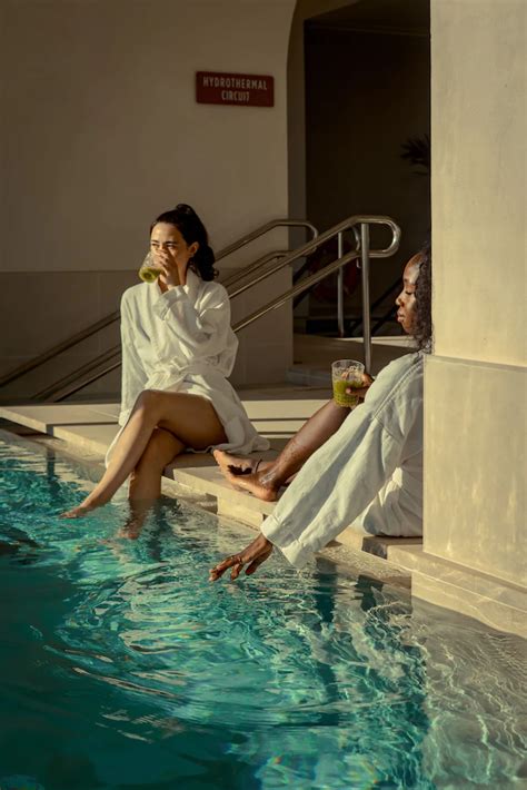 Two Women Sitting On The Edge Of A Swimming Pool One Holding A Drink