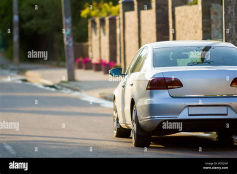 Close-up back view of new shiny expensive silver car moving along city street on blurred trees ...