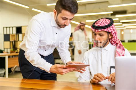 رجل اعمال سعودي خليجي باللباس السعودي التقليدي يجلس على مكتبه و يستخدم