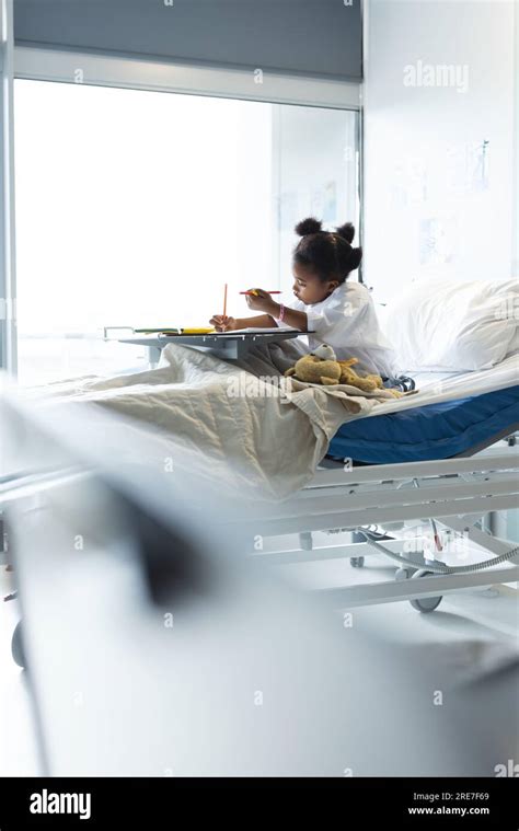 African American Girl Patient Lying On Bed Colouring In Patient Room At