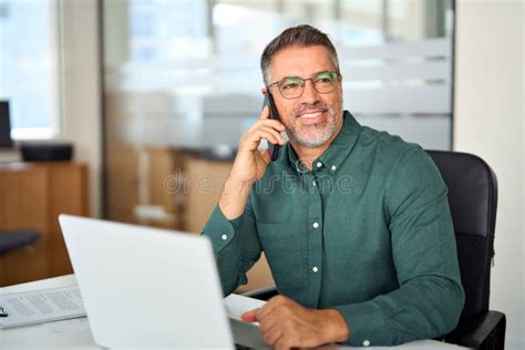 Smiling Mature Businessman Making Call On Cellphone Working In Office