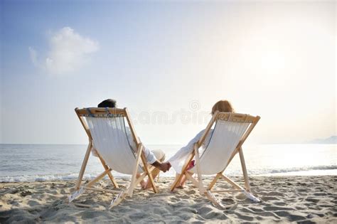 Romantic Couple On Deckchair Relaxing Enjoying Sunset On The Beach