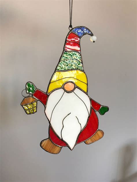 A Stained Glass Christmas Ornament With A Gnome Holding A Basket Of Ts Hanging From It S Side