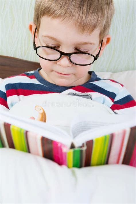 Livro De Leitura Bonito Pequeno Do Menino Na Cama Foto De Stock