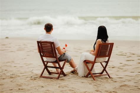 Vista Traseira De Um Casal Bebendo Sentado Em Cadeiras Na Praia Foto